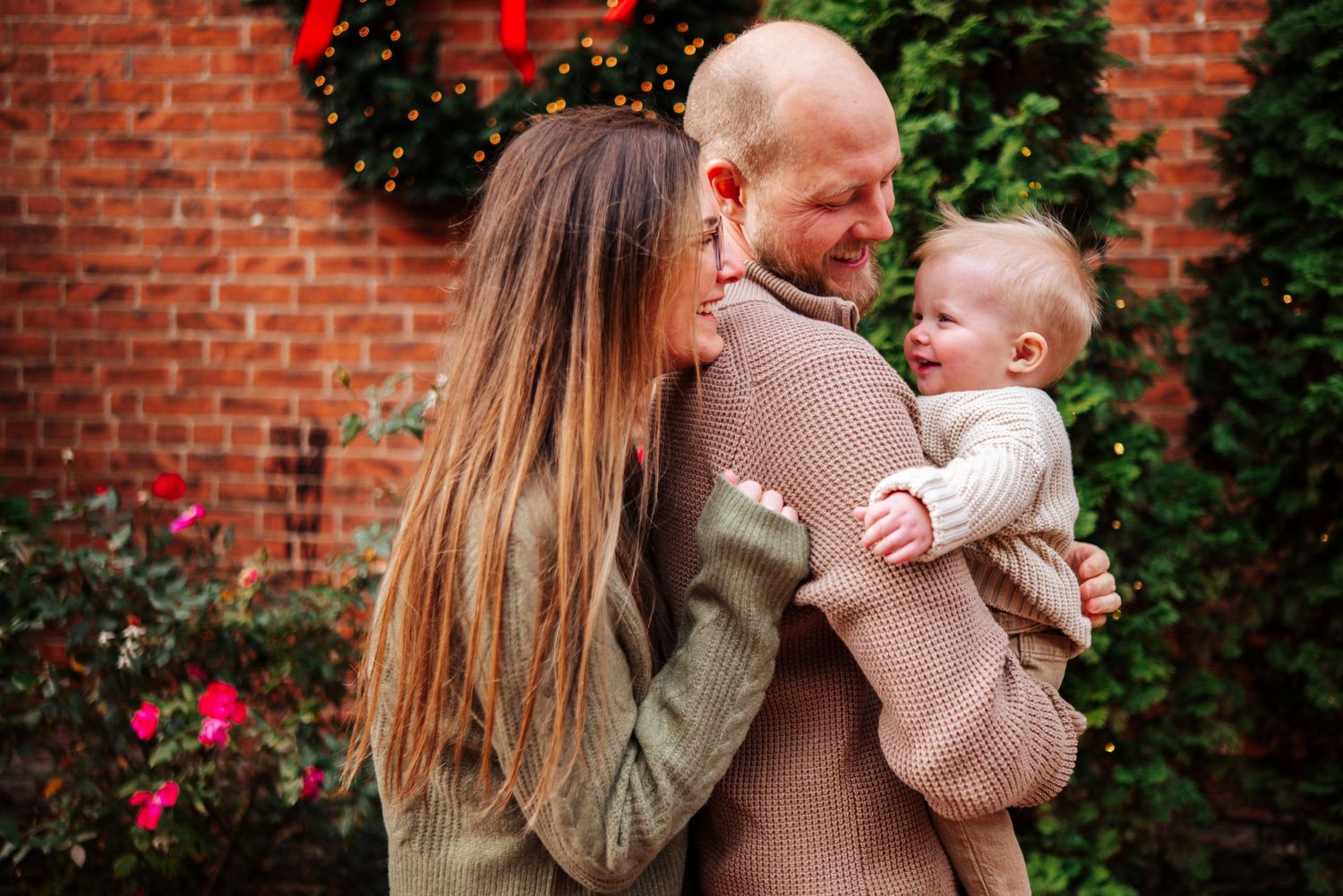 A series of candid outdoor family moments captured against a brick wall with greenery and pink flowers.