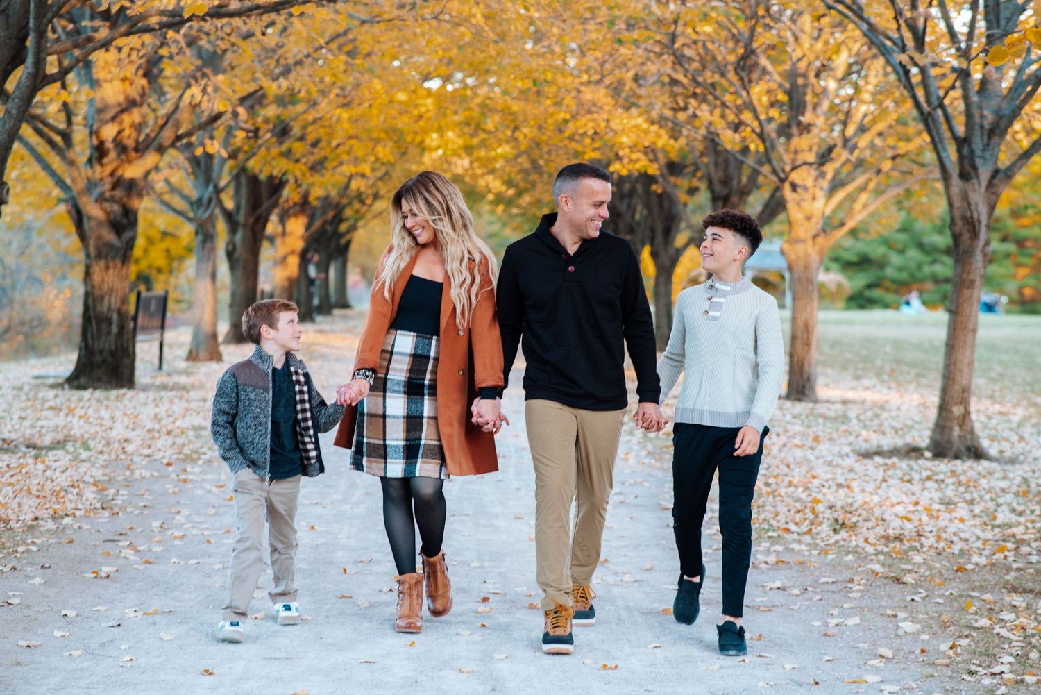 Group of people walking along autumn path with golden yellow leaves scattered on ground in park setting at the Toledo Botanical Gardens.