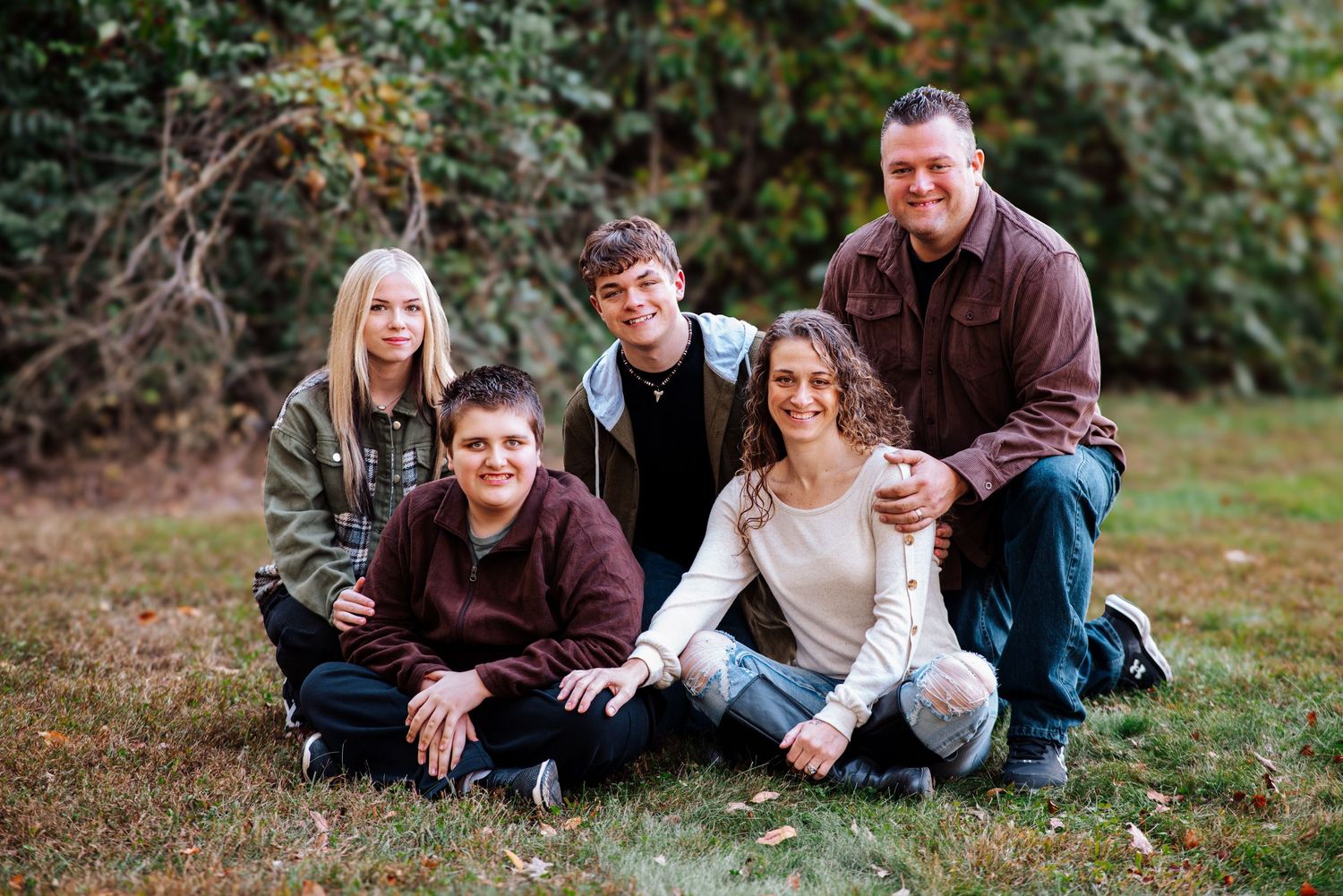 A group sits together on grass during an outdoor autumn photo session in casual clothing.