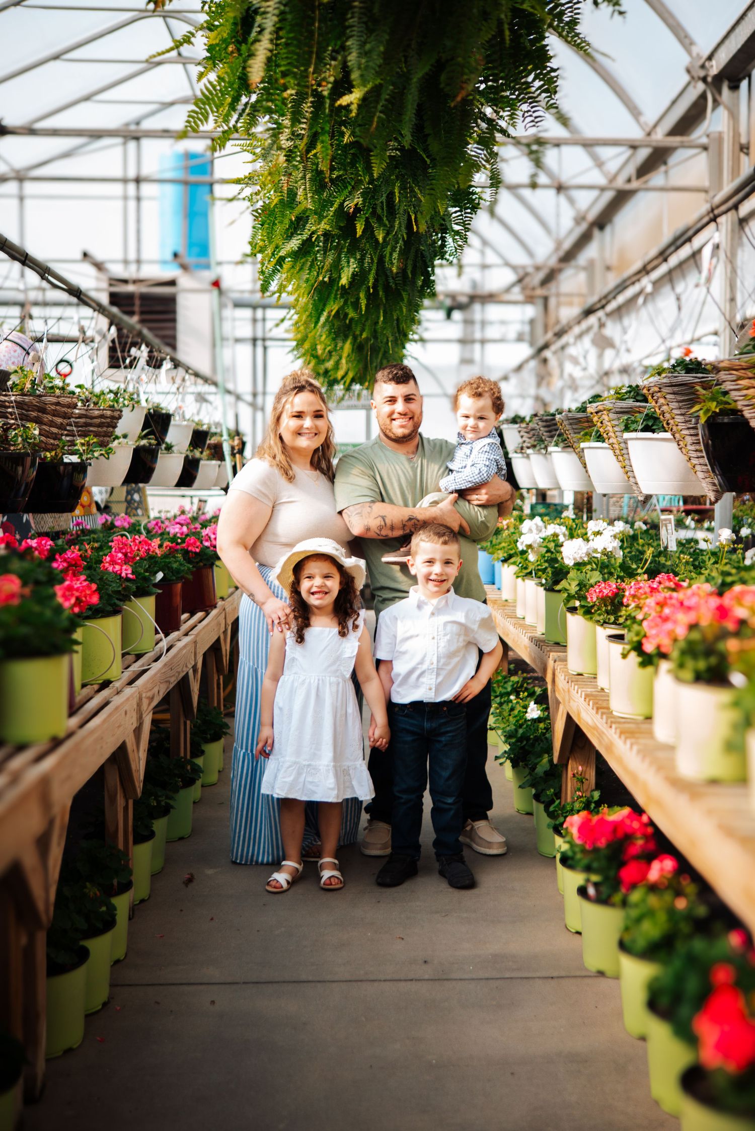 Family posing together in a greenhouse walkway surrounded by colorful flowers and hanging plants.