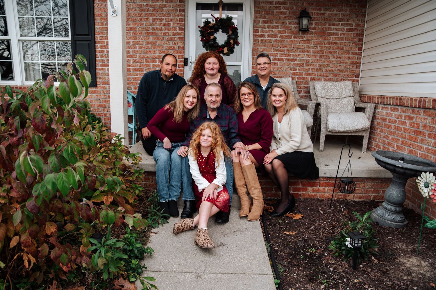 A group sits together on brick steps in front of a house during a fall photo session celebrating end of life.