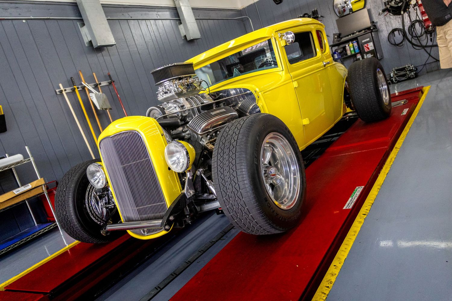 A bright yellow vintage hot rod car with chrome details displayed at an indoor auto show from multiple angles.