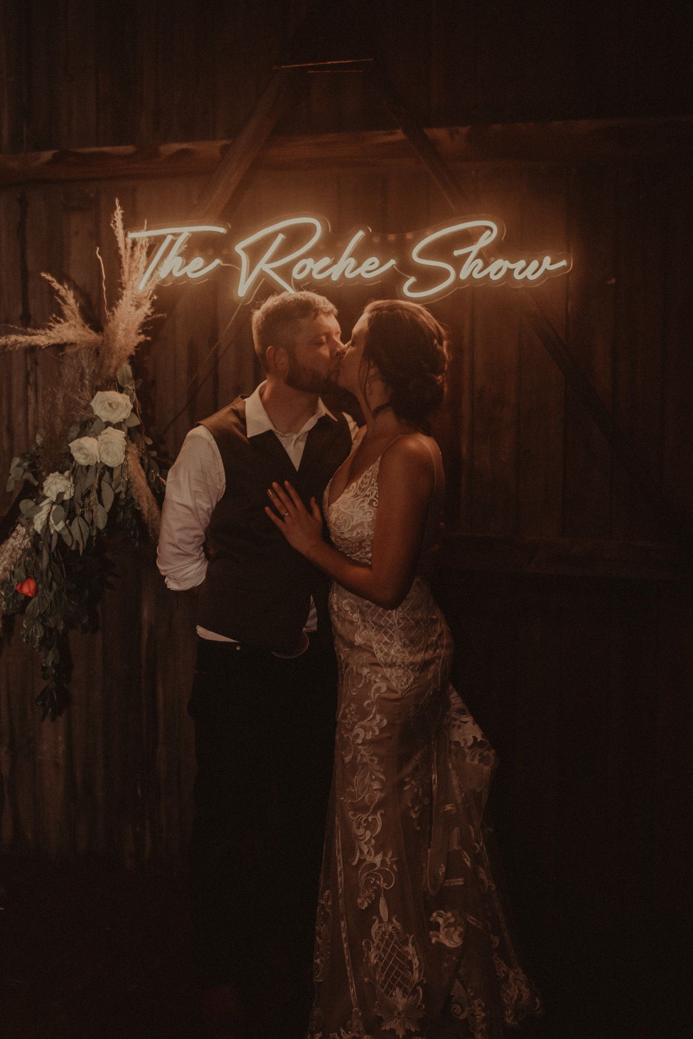 A couple shares a romantic dance moment in a dimly lit reception venue with elegant decor and neon signage.