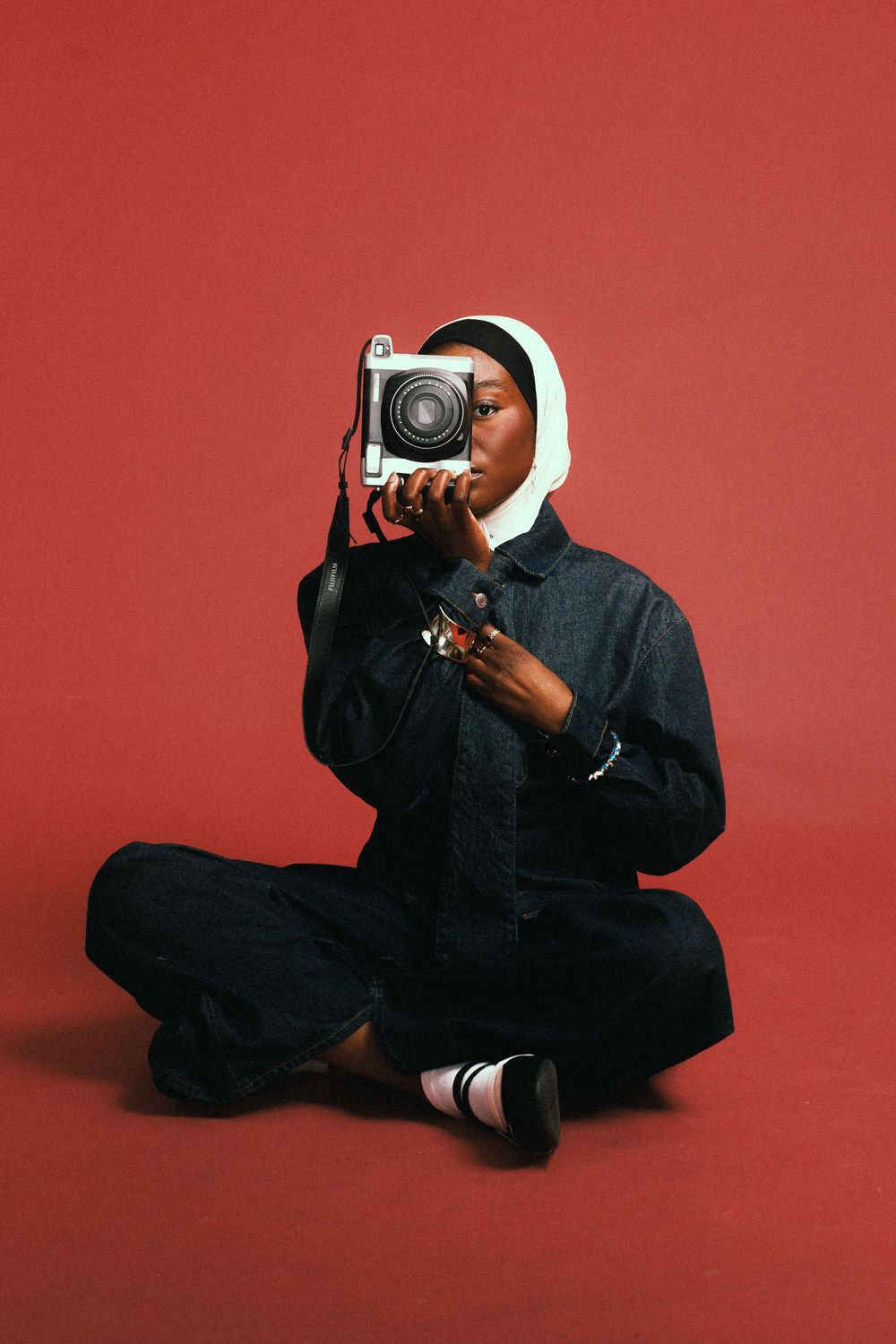 Photographer in black clothing lying on red backdrop while taking photos from creative low angles.