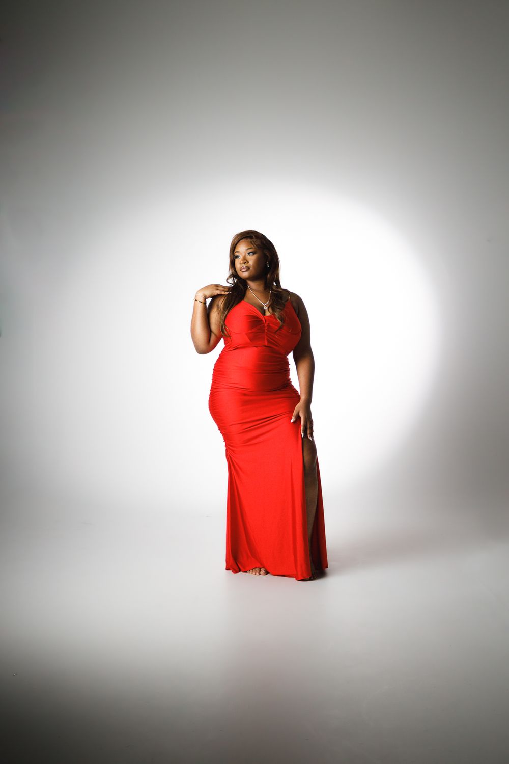 A plus size figure in a flowing red dress poses confidently against a white studio backdrop in a series of shots.