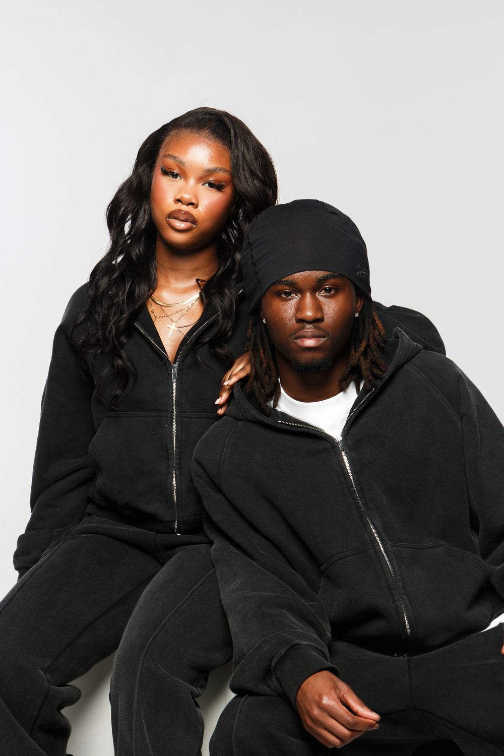 Four artistic fashion photos show models in matching black hooded sweatshirts posing against a white backdrop.