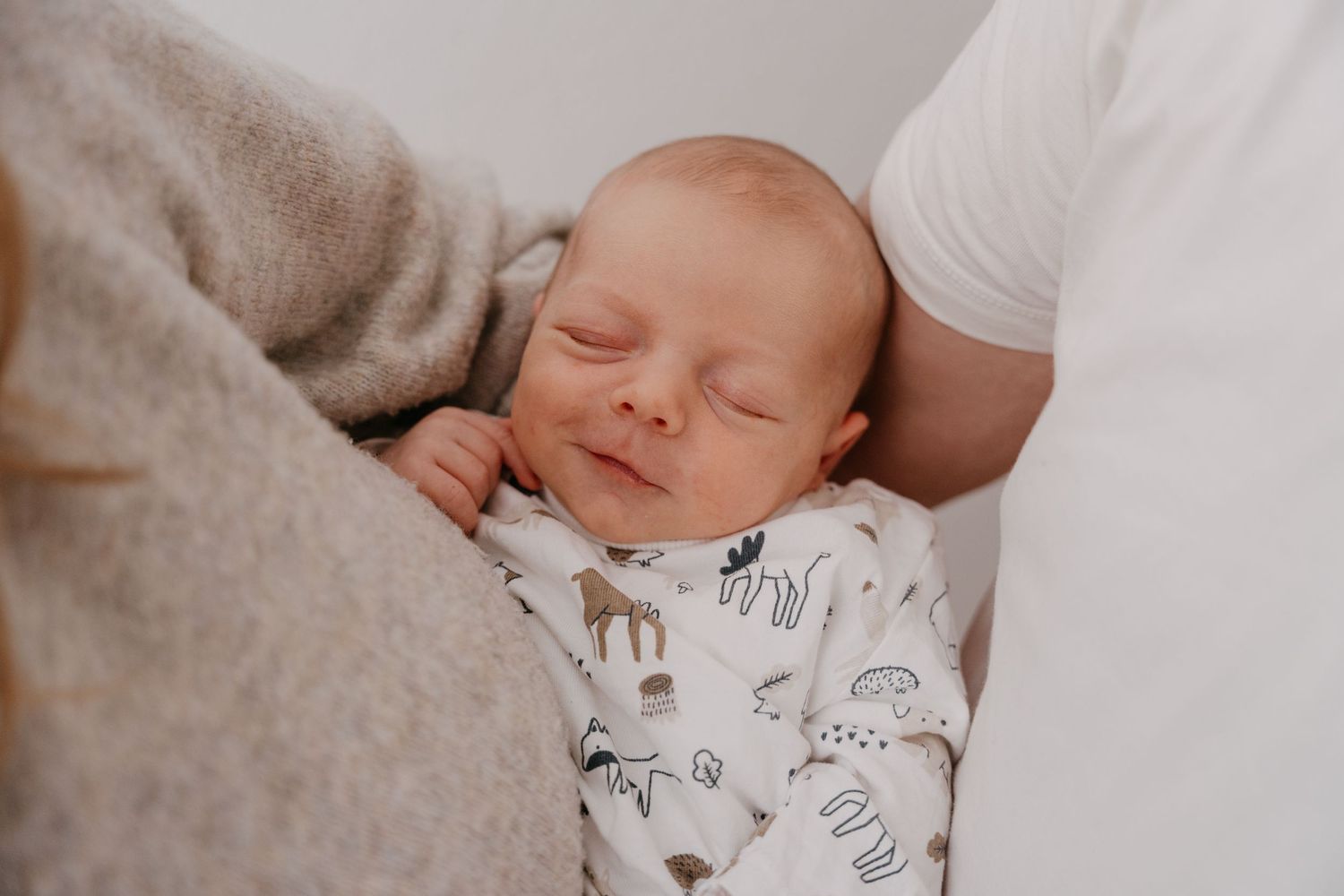 A sleeping newborn baby wearing an animal print onesie rests peacefully on a soft white blanket.