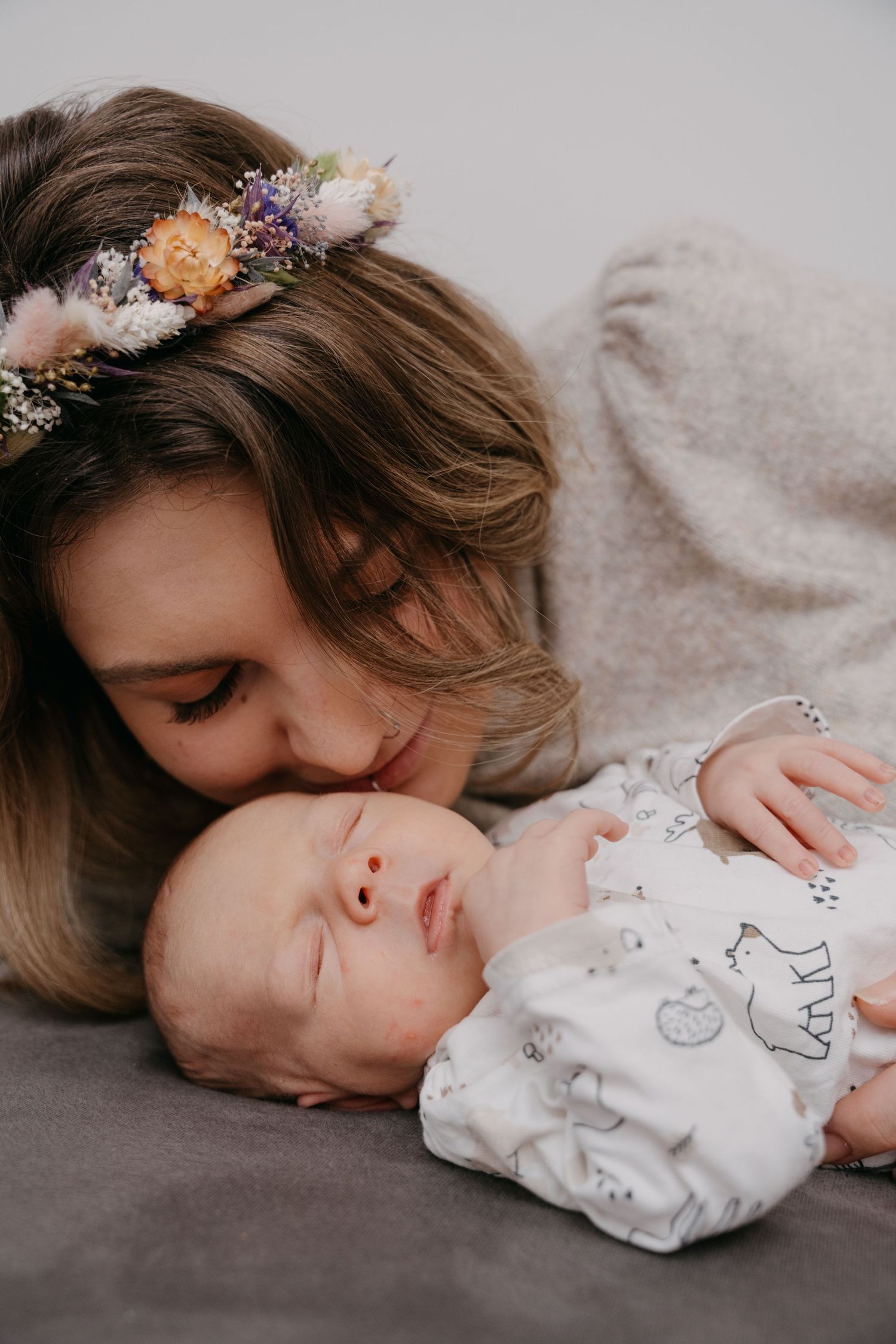 A tender moment captured between a sleeping baby in a patterned onesie and someone wearing a delicate floral crown.