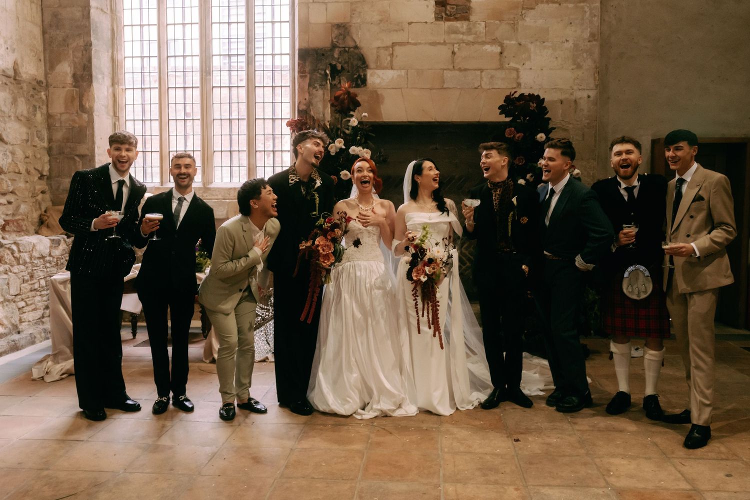 Wedding party members stand in a row against a rustic brick wall during a formal celebration ceremony.