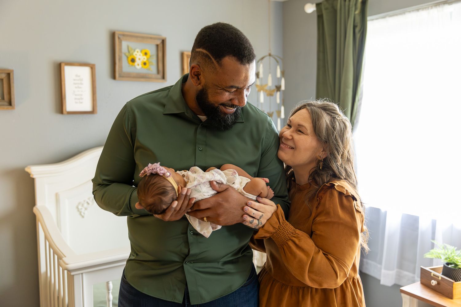 Happy parents smile lovingly at their newborn baby in a softly decorated nursery room.