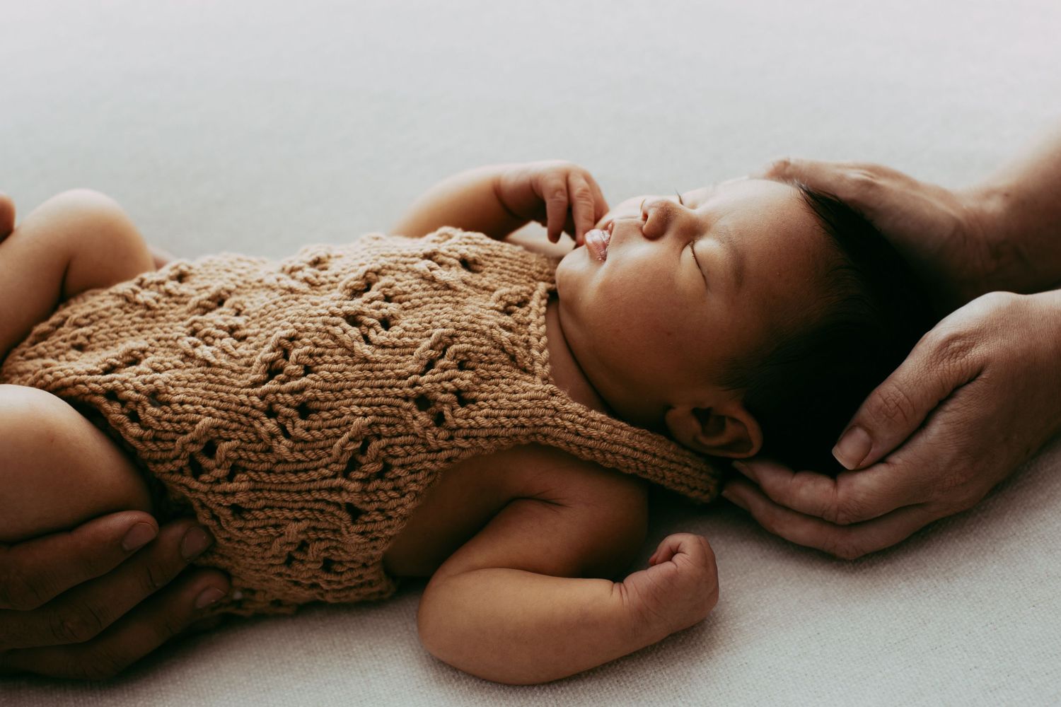 Artistic side view of baby wearing knitted cream outfit against light background.