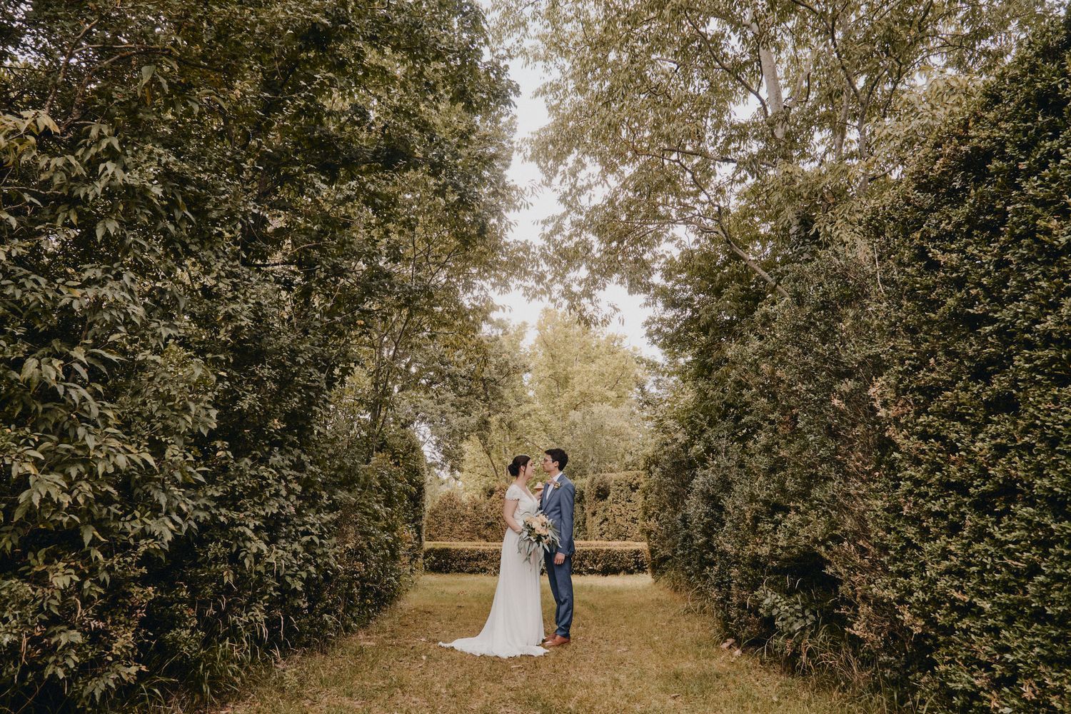 Wedding couple photographed in a tree-lined path creating a natural tunnel effect.