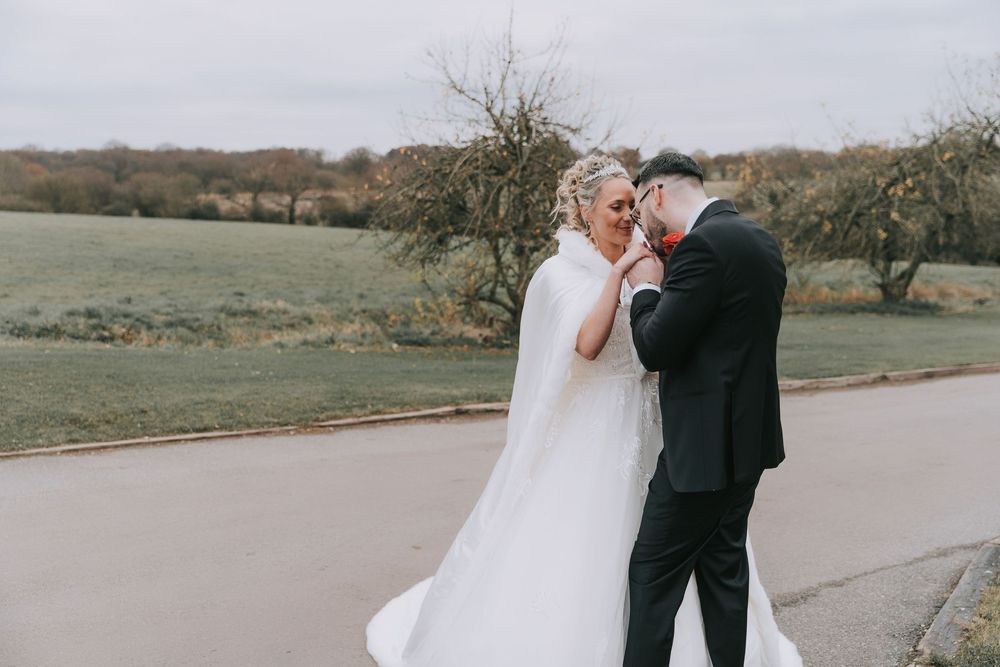 A couple shares an intimate moment on their wedding day on a paved path surrounded by autumn trees.