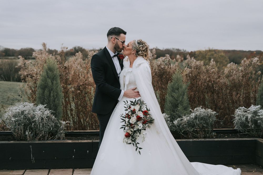 A romantic outdoor wedding scene with the couple embracing against a scenic natural backdrop at sunset.