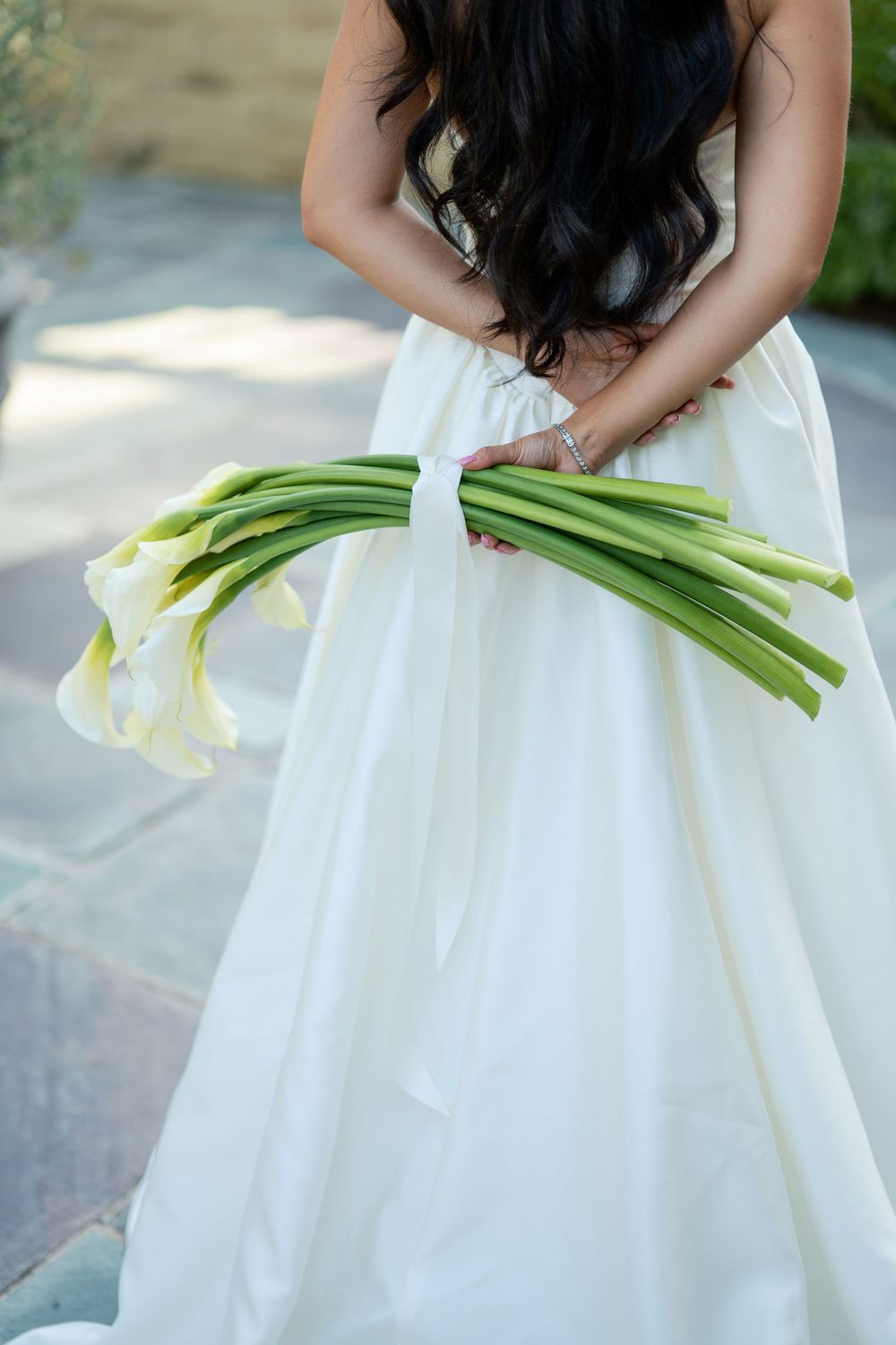 A bride in a white dress holds an elegant bouquet of white calla lilies against her flowing gown.