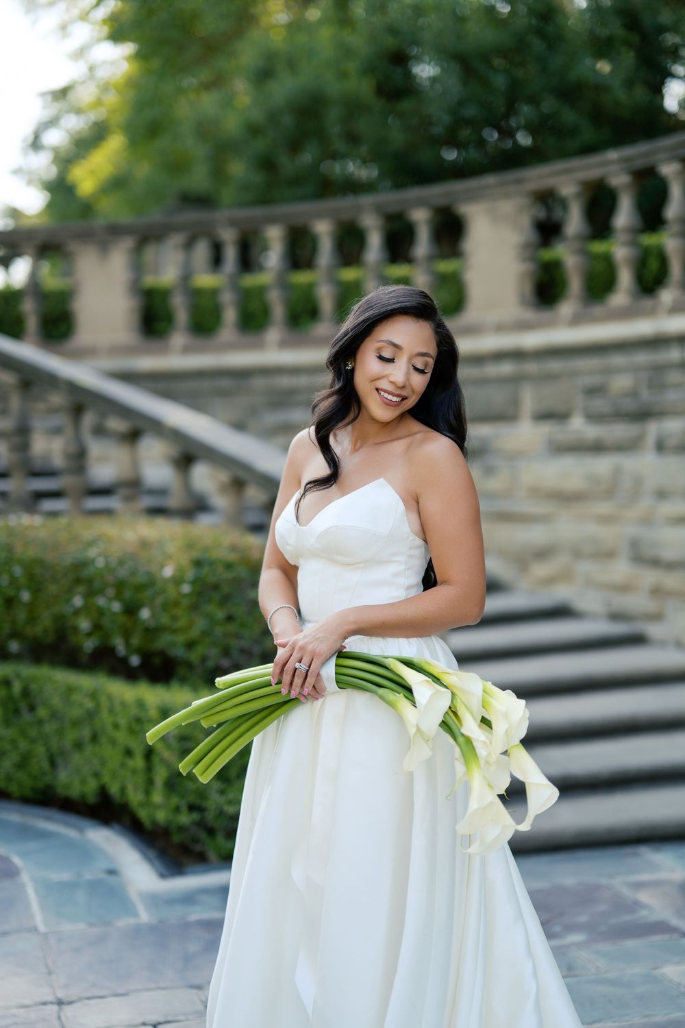 A white wedding gown and calla lily bouquet create an elegant bridal portrait on stone steps.