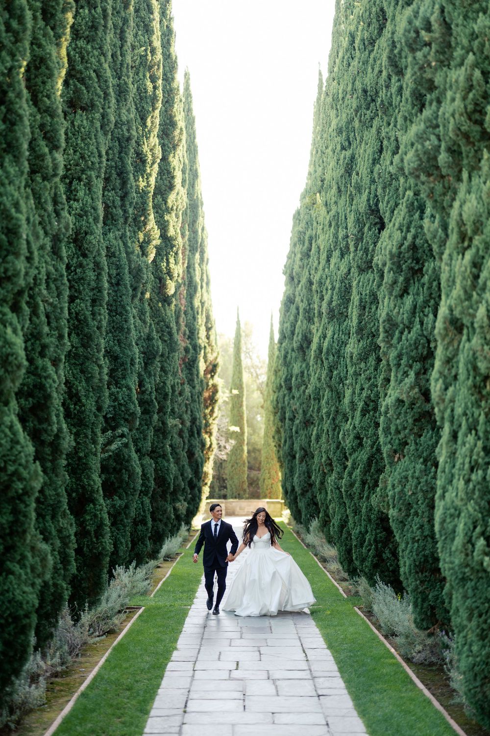 Wedding couple walks down a majestic cypress tree-lined pathway with stone pavers.