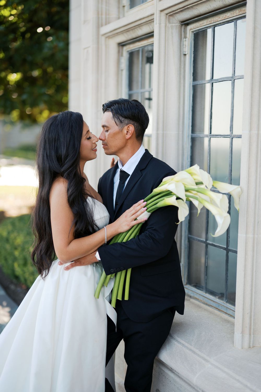 A romantic wedding moment captured against a classic white building with large windows.