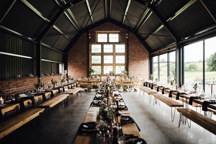 Industrial-style event space with exposed beams and long wooden communal tables.