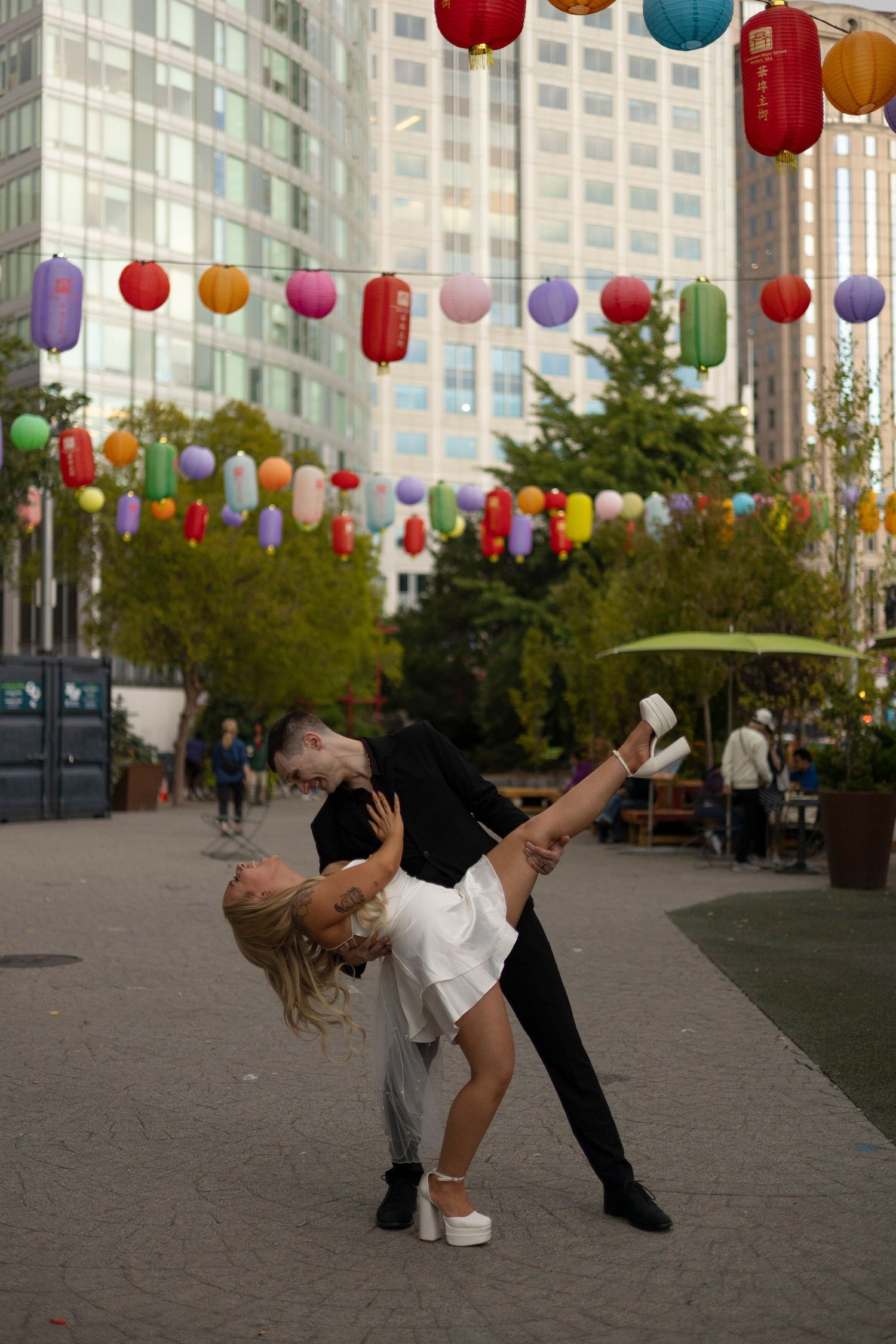 A dance sequence under colorful paper lanterns shows a graceful dip move between two performers on a city plaza.