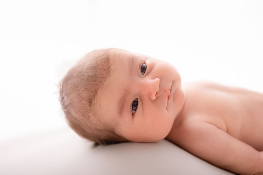 Newborn baby lying on white background, looking up with bright eyes in a soft, peaceful portrait photo. Newborn Photographer Michigan