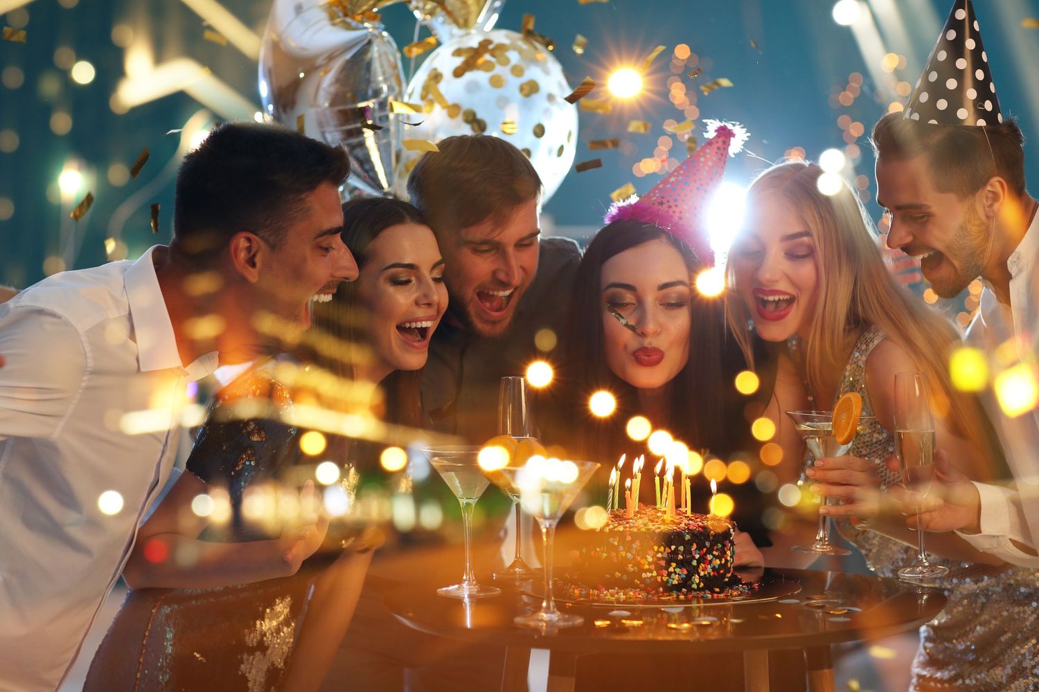 A group of friends celebrating at a dinner party with glowing candles and festive lights in the background.