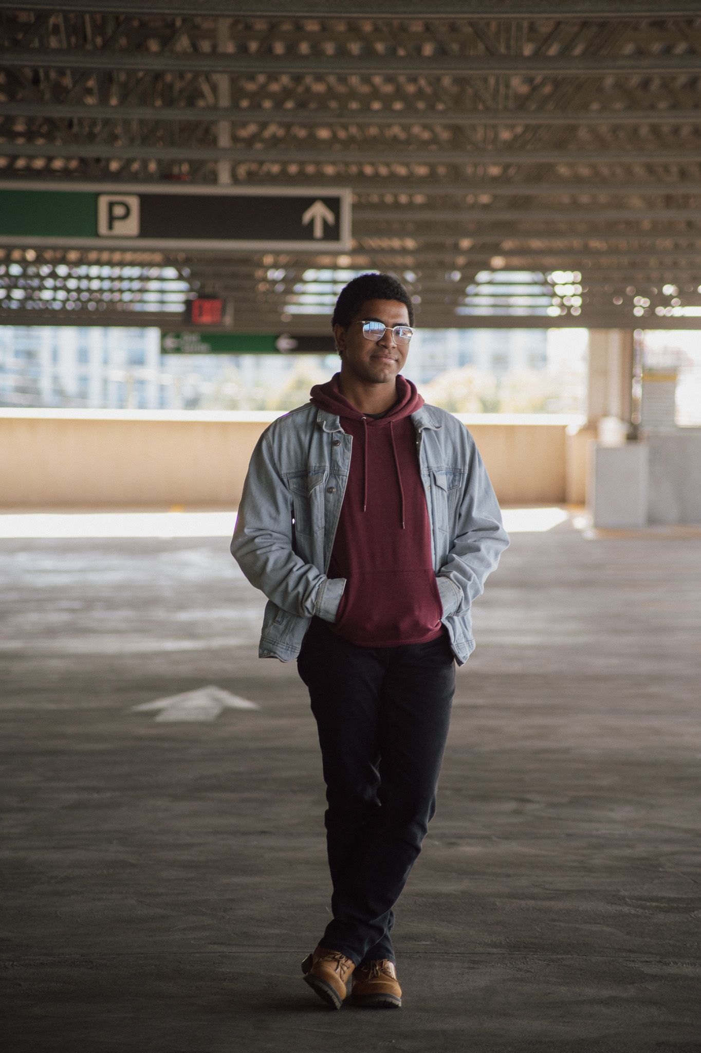 Person in denim jacket and burgundy hoodie standing in an empty concrete parking garage.