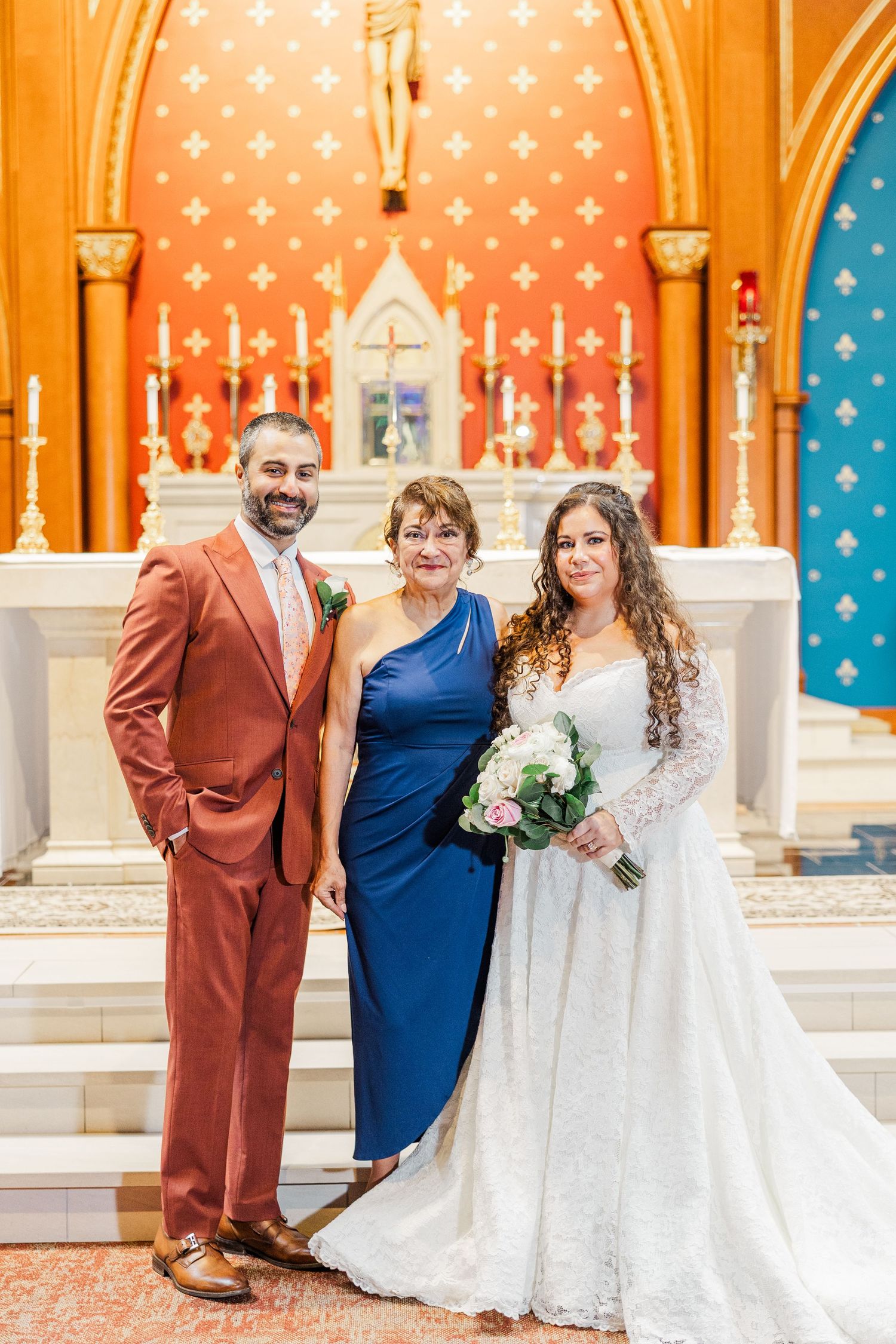 Wedding party poses in church with ornate orange and blue patterned walls and altar.