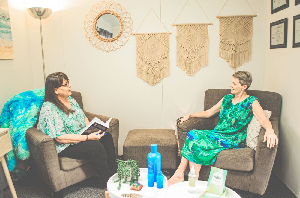 Two people in matching green dresses sit in armchairs having a conversation in a decorated room.
