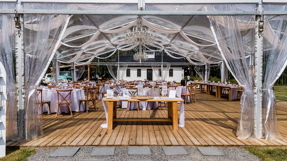 Elegant outdoor wedding reception setup under a white draped tent with wooden deck flooring and rustic table settings.