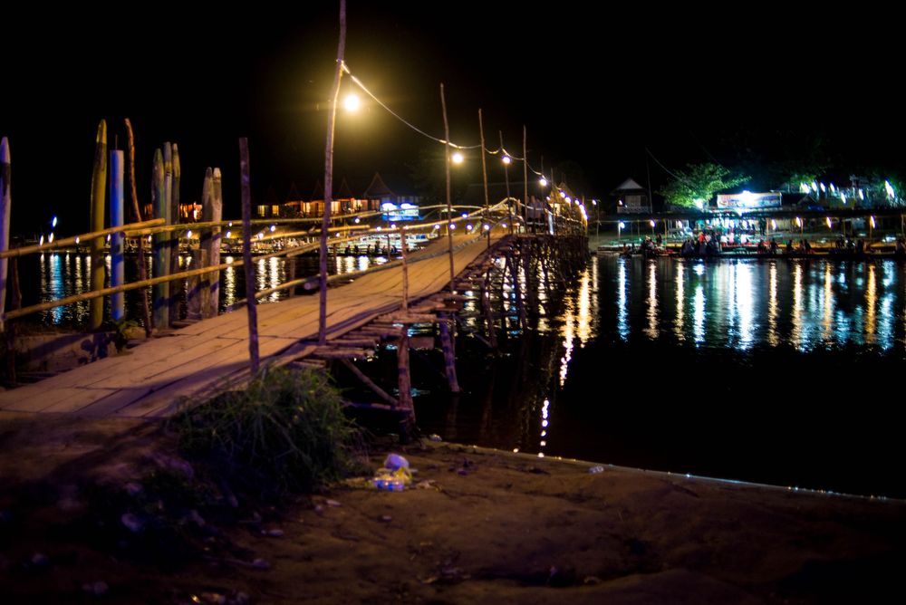 Illuminated wooden dock and marina at night with lights reflecting on calm water.