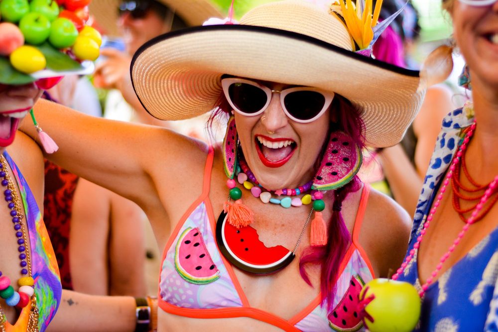Group of people in colorful summer outfits and sunhats enjoying a festive beach party with tropical drinks.