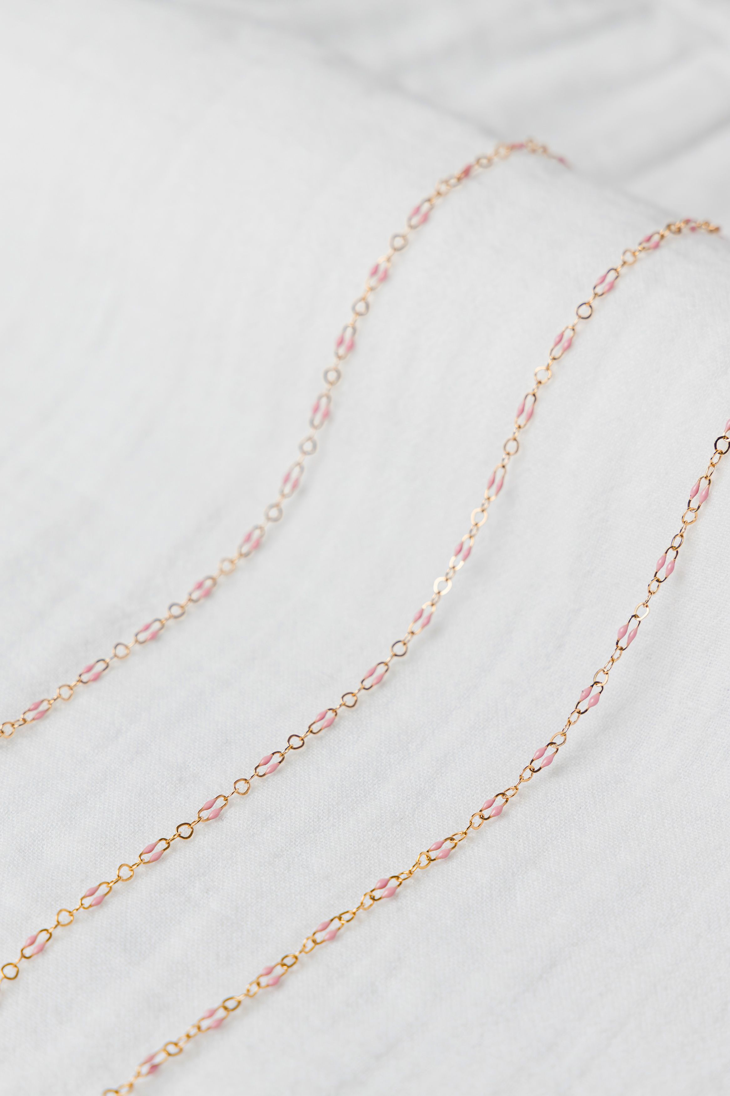 Delicate pink enamel permanent jewelry chain photographed in soft neutral luxury studio setup in Jupiter Florida.