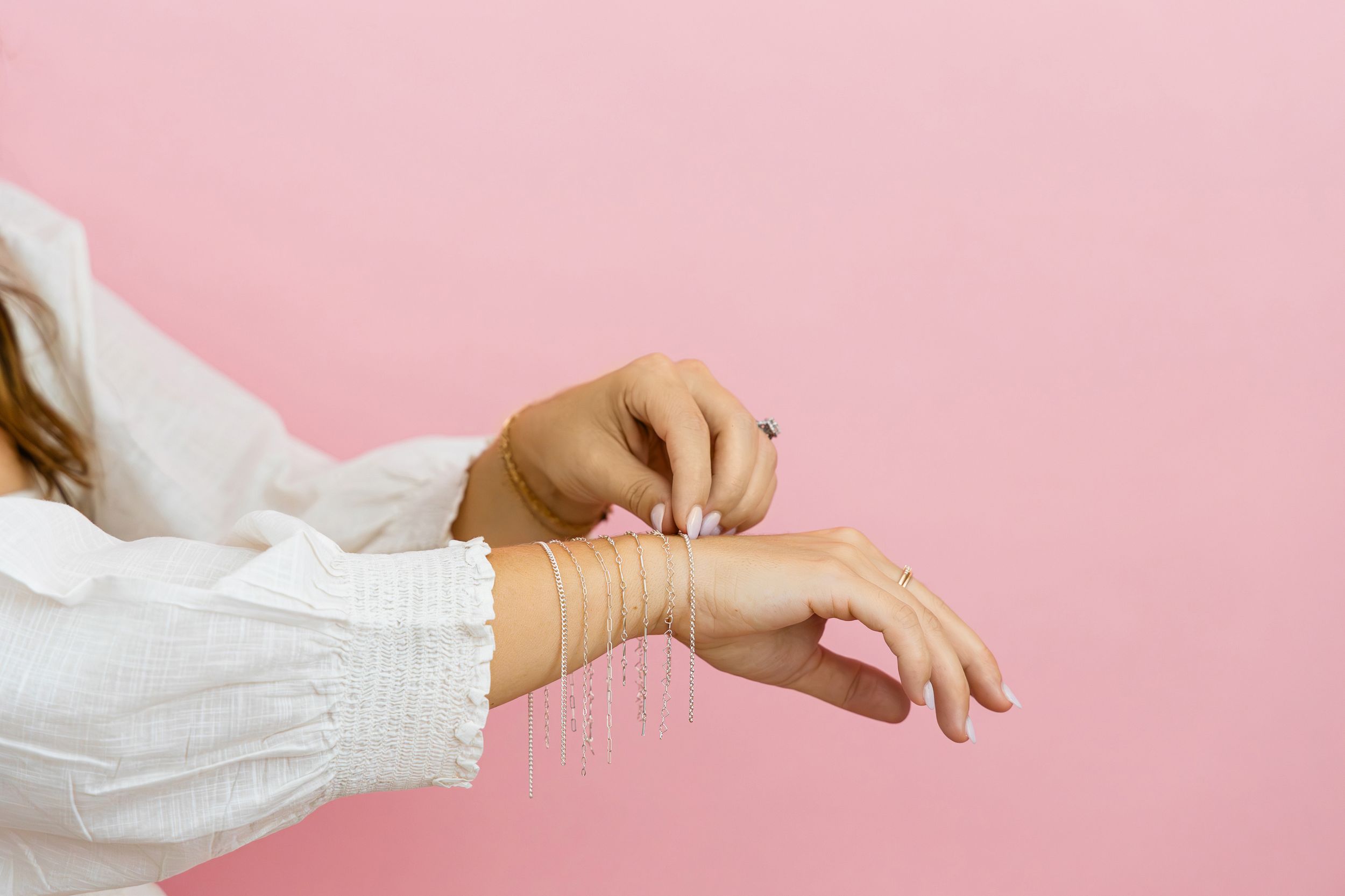 Permanent jewelry bracelets styled on wrist against pink backdrop in luxury jewelry brand photography in Jupiter Florida.