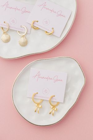 Gold bow earrings photographed on branded jewelry cards in feminine luxury product photography in Jupiter Florida.
