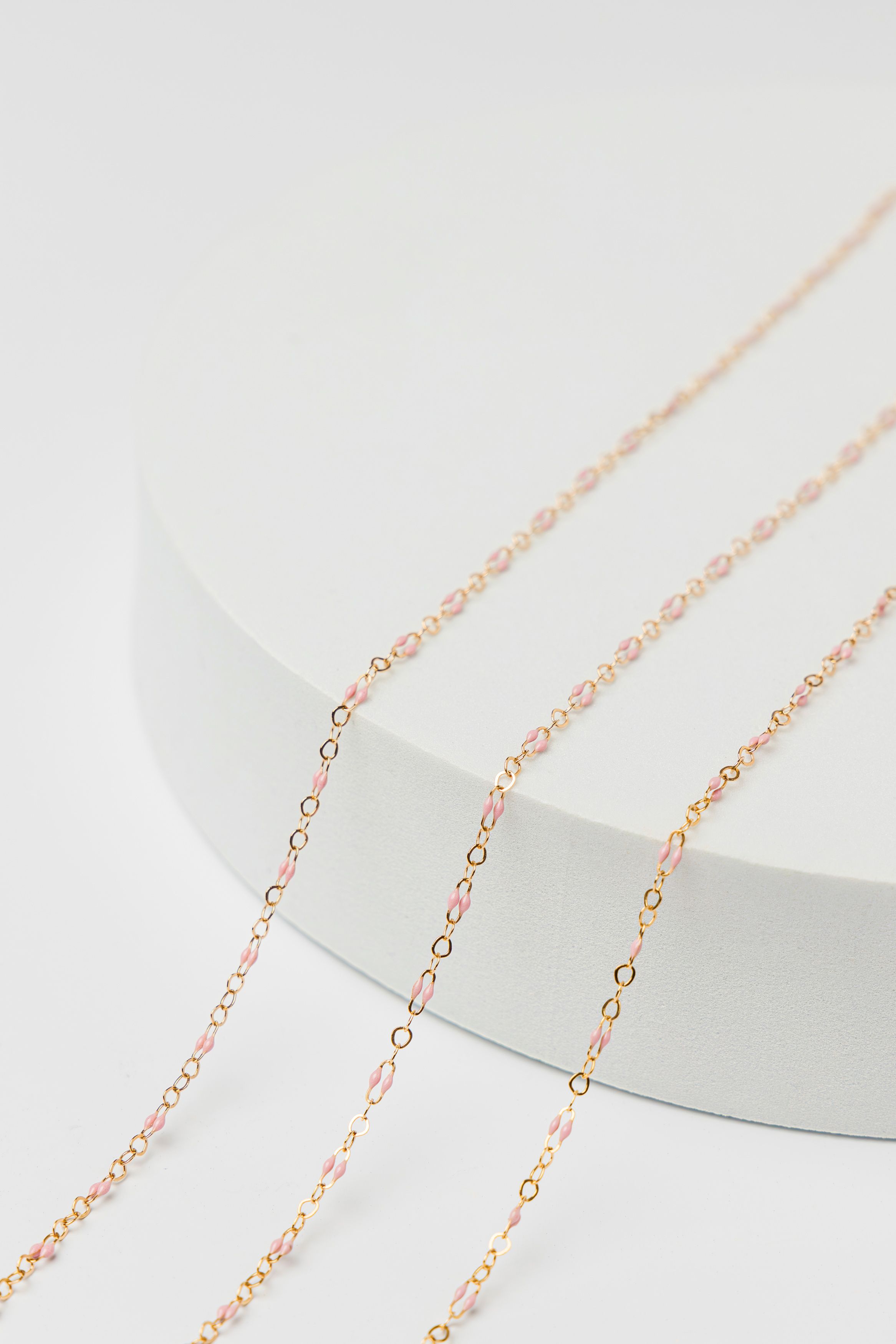 Pink and gold enamel permanent jewelry chain styled in minimal feminine luxury product photography in Jupiter Florida.