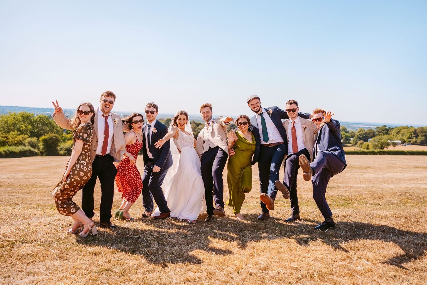 Wedding party poses together on a sunny hillside in a fun and playful manner during golden hour.