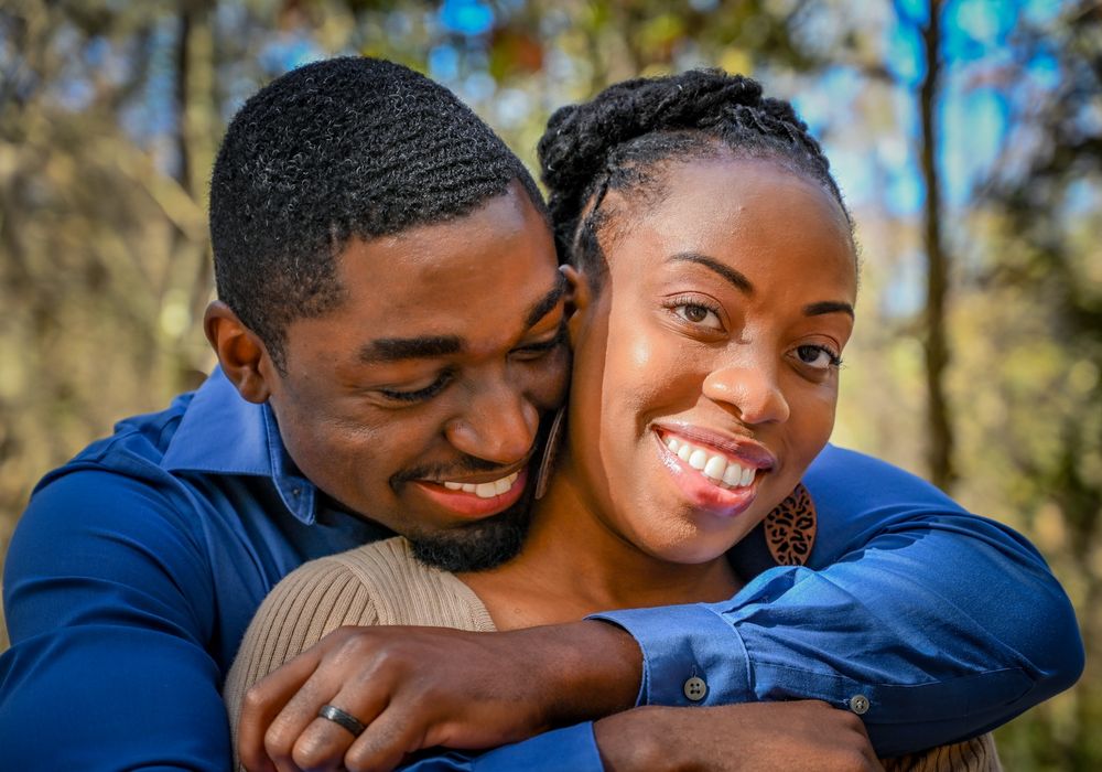 A happy couple shares tender moments and laughter while embracing outdoors in a natural setting.