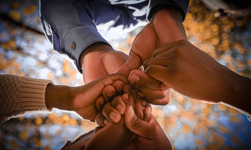 Hands of diverse people joining together in unity against blurred autumn background.