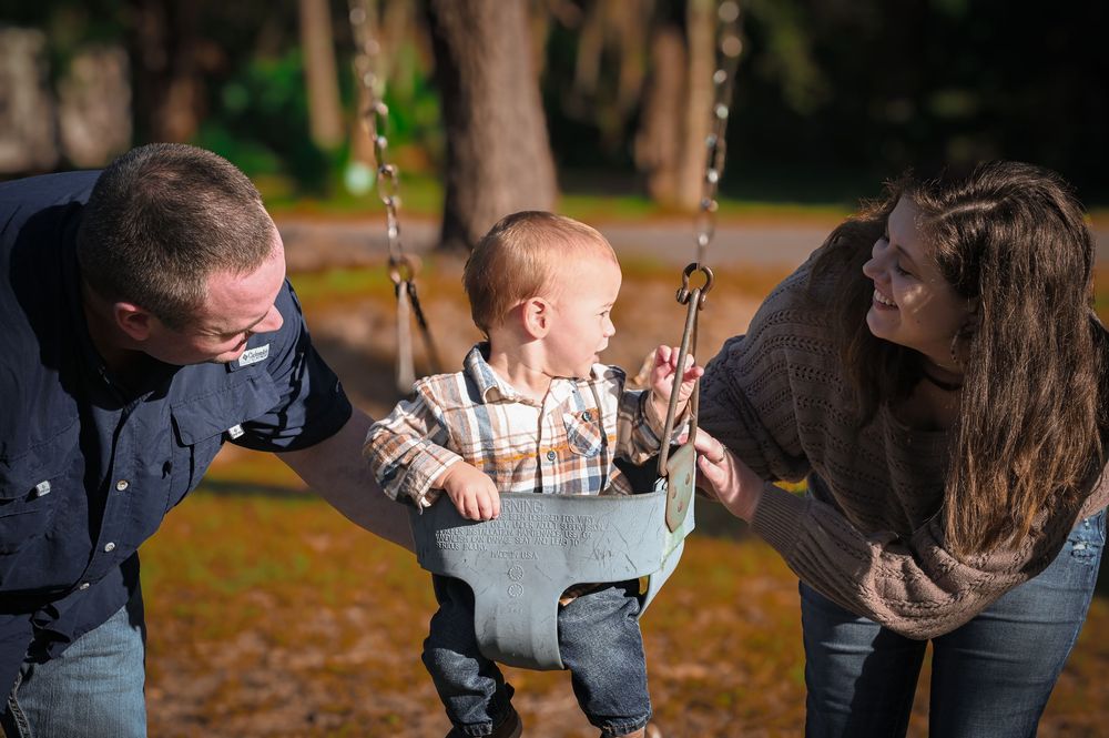 A person swings on a playground swing set in an autumn park setting with fallen leaves on the ground.