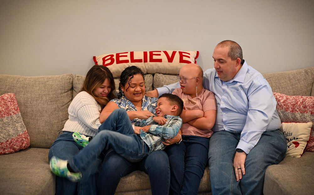 A family sits together on a beige couch, sharing laughter and playful moments in their living room.