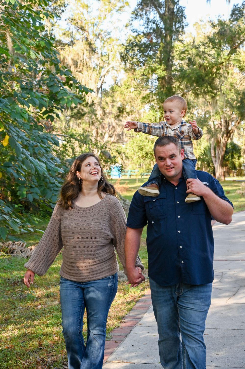 A couple walks together on a tree-lined path while laughing and enjoying a sunny autumn day.