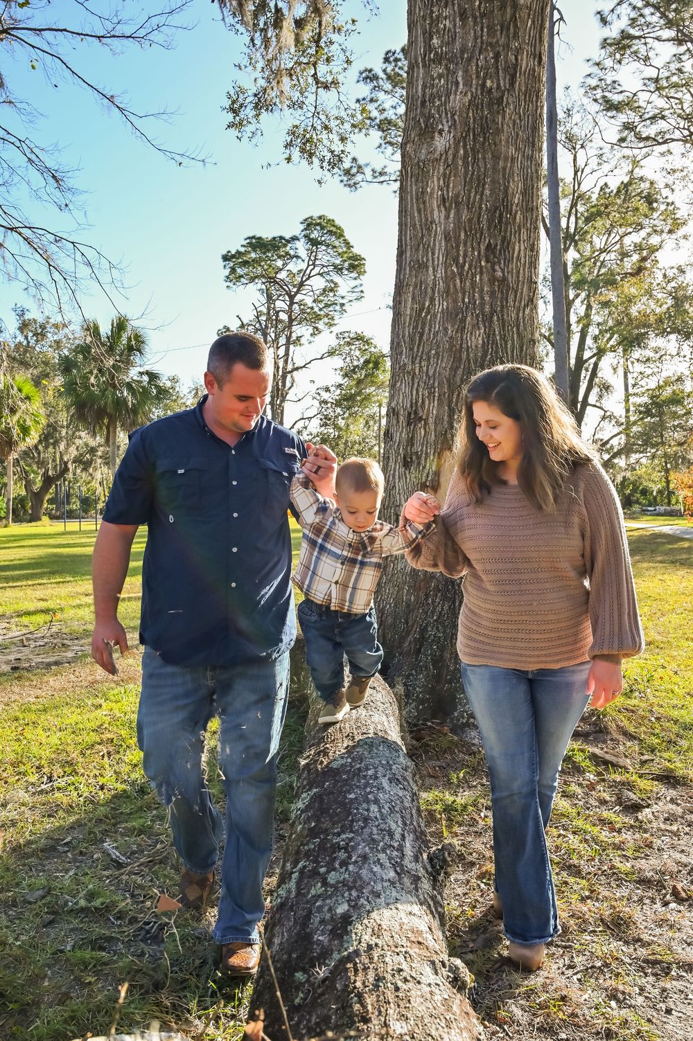 A family explores a wooded area together on a sunny afternoon, examining something interesting on a tree trunk.