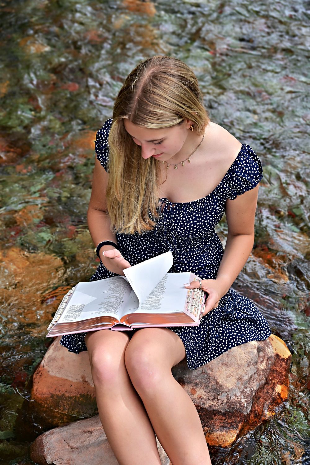 senior portrait of a girl sitting on a rock in the middle of a crystal clear stream reading a bible glacier national park montana