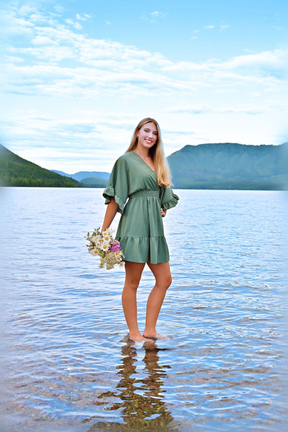 senior portrait of a girl standing in the water of lake McDonald holding a bouquet of wildflowers glacier national park montana