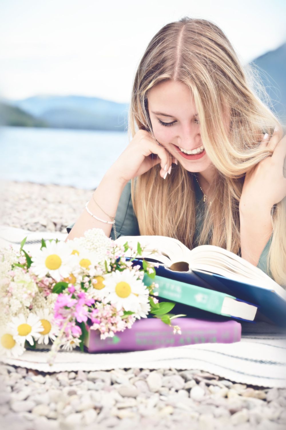 senior portrait of a girl reading books with wildflowers laughing on the shore of lake McDonald glacier national park