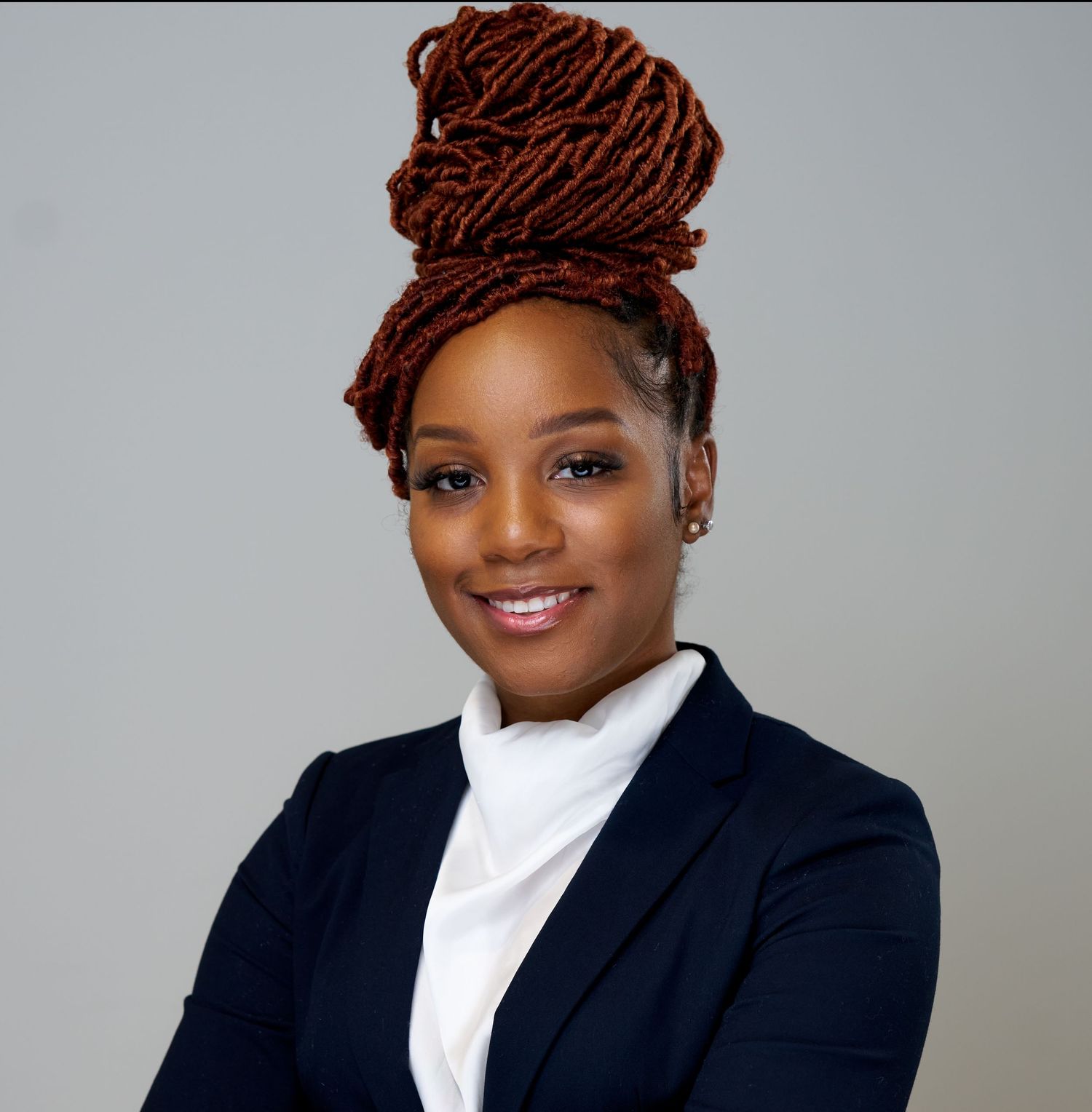 Professional headshots of person with red locs wearing navy blazer and white top.