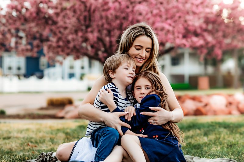 Family enjoying a playful moment together under blooming pink cherry blossom trees in a spring garden setting.