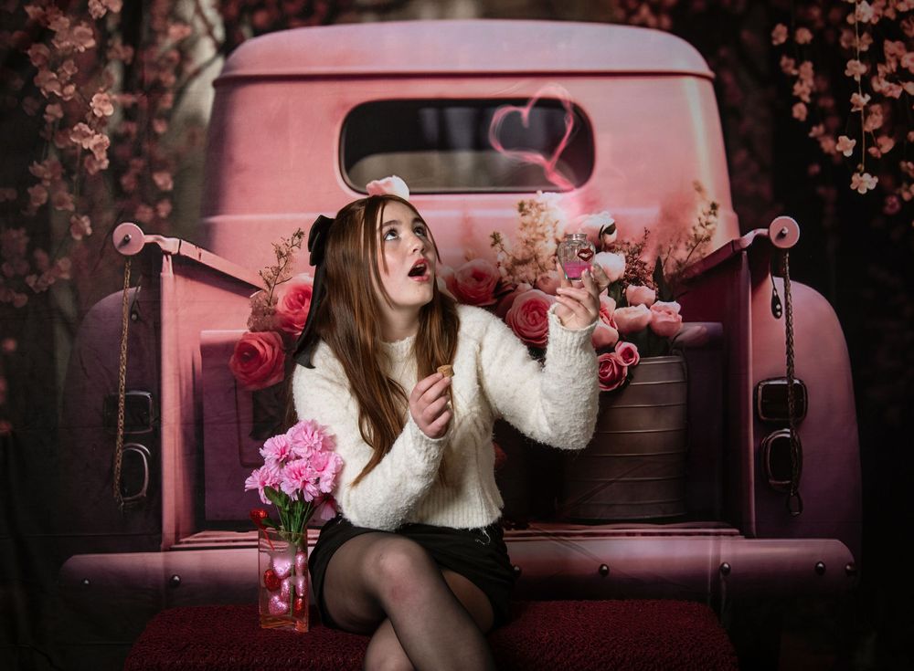 A romantic Valentine's Day photo session featuring people on a vintage couch with floating heart decorations and pink lighting.