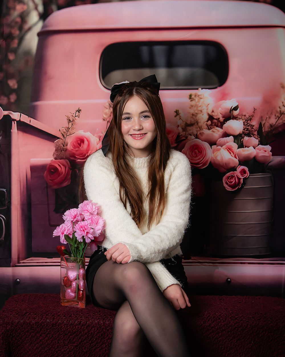 Pink vintage truck backdrop with roses and white sweater against romantic floral setting.